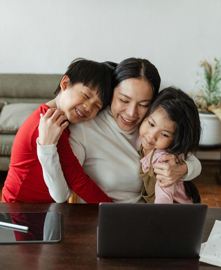 A mother embraces her children while working from home, blending family time with remote work.